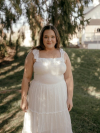 Leslie Harker wearing white dress standing under evergreen tree